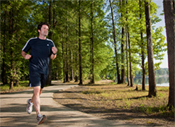 Man wearing black t-shirts and shorts jogging on a forest track